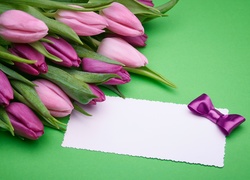 Bukiet fioletowych tulipanów obok białej karteczki z kokardką