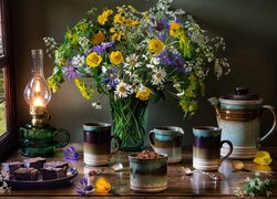 Bukiet kwiatów obok lampy, ciasta i kubków do kawy