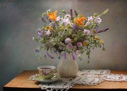 Bukiet polnych kwiatów w wazonie obok filiżanki herbaty