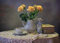 Bukiet róż w dzbanku obok książek i porcelanowej figurki na stoliku