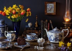 Bukiet żonkili i tulipanów obok serwisu do kawy i lampy