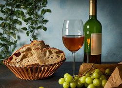 Butelka i kieliszek wina obok winogron i chleba w koszyku