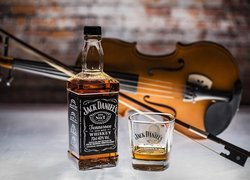 Butelka whisky Jack Daniels obok szklanki i skrzypiec