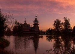 Cerkiew i drzewa nad jeziorem o zachodzie słońca