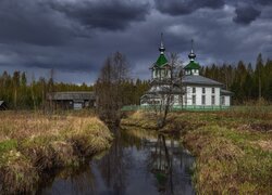 Cerkiew nad rzeką pod ciemnymi chmurami