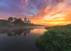 Cerkiew nad zamgloną rzeką w blasku wschodzącego słońca