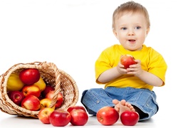 Chłopczyk z jabłkiem w dłoniach obok kosza z jabłkami