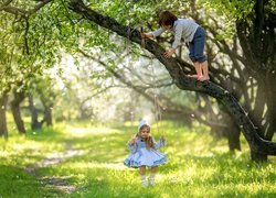 Chłopiec na drzewie i dziewczynka na huśtawce