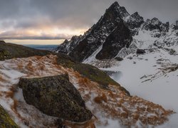 Chmury nad ośnieżonymi górami i trawami na skałach w śniegu