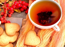 Ciasteczka w kształcie serc położone obok jarzębiny i filiżanki z herbatą
