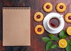 Ciastka i cytryny obok herbaty w filiżance i notesu