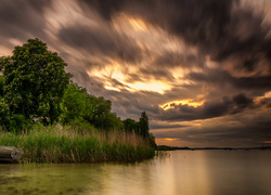 Ciemne chmury nad rzeką i łódką w szuwarach o świcie