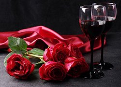 Czerwone róże obok kieliszków z winem