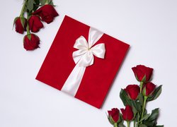 Czerwone róże obok prezentu przewiązanego wstążką