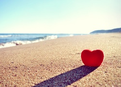 Czerwone serce w piasku na morskiej plaży