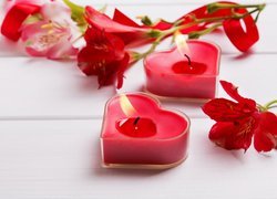 Czerwone świeczki serduszka obok kwiatów