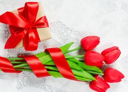 Czerwone tulipany obok prezentu z kokardą