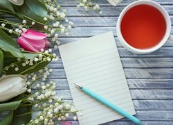 Długopis na kartce obok wiosennych kwiatów i herbaty