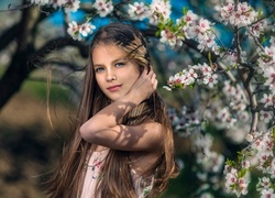 Długowłosa dziewczynka pozuje do zdjęcia pod drzewem owocowym