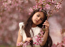 Długowłosa dziewczynka stoi obok kwitnącego drzewa