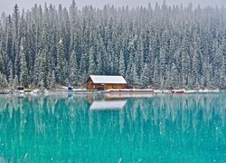 Dom pod ośnieżonym lasem nad brzegiem jeziora Louise Lake