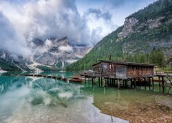 Domek na pomoście i szereg łodzi na jeziorze Lago di Braies i w zamglonych Dolomitach