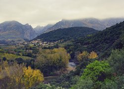 Domy i rzeka w dolinie na tle zamglonych gór