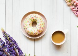 Donut na talerzyku obok filiżanki z kawą i łubinu