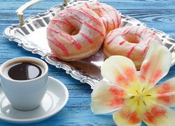 Donuty na tacy obok filiżanki kawy i rozwiniętego tulipana