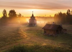 Drewniana kaplica obok domku w zamglonej wsi