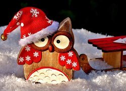 Drewniana sowa w czapce Mikołaja z saniami na śniegu