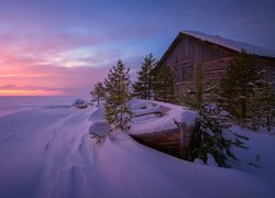 Drewniany dom obok zasypanej śniegiem łódki o zachodzie słońca
