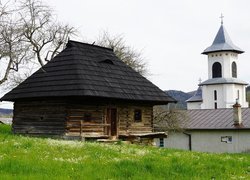 Drewniany dom pod bezlistnym drzewem obok kościoła