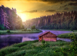 Drewniany domek nad brzegiem rzeki o zachodzie słońca