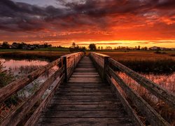 Drewniany most nad rzeką pod kolorowym niebem zachodzącego słońca