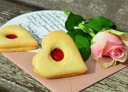 Dwa ciasteczka w kształcie serca obok róży na kopercie