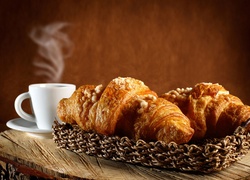 Dwa croissanty w koszyczku obok parującej kawy w filiżance
