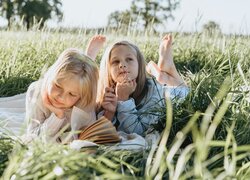 Dwie dziewczynki leżące z książką na łące