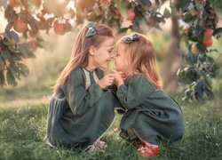 Dwie dziewczynki pod gałęziami jabłoni