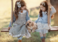 Dwie dziewczynki siedzące na huśtawce ze szczeniaczkiem