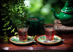 Dwie herbaty w szklankach z zielonym imbrykiem w tle