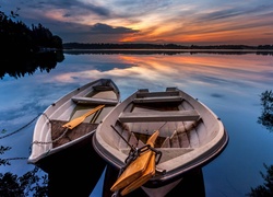 Dwie łódki na brzegu jeziora o zachodzie słońca