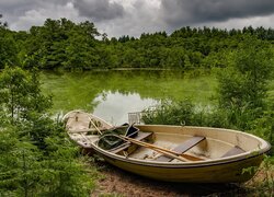 Dwie łódki na brzegu stawu otoczonego drzewami