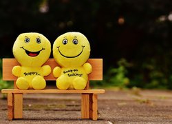 Dwie żółte uśmiechnięte maskotki na ławeczce