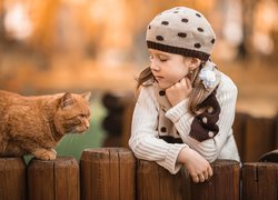 Dziewczyna i rudy kot przy płocie