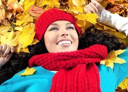 Dziewczyna w czapce i szaliku leży na jesiennych liściach