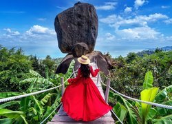 Dziewczyna w czerwonej sukni na kładce z widokiem na skałę