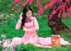 Dziewczyna w różowej sukience na kocu pod kwitnącym drzewem