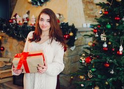 Dziewczyna z prezentem obok świątecznej choinki