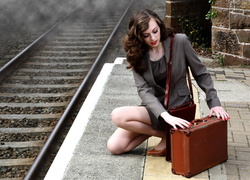 Dziewczyna z walizką na peronie przy torach kolejowych